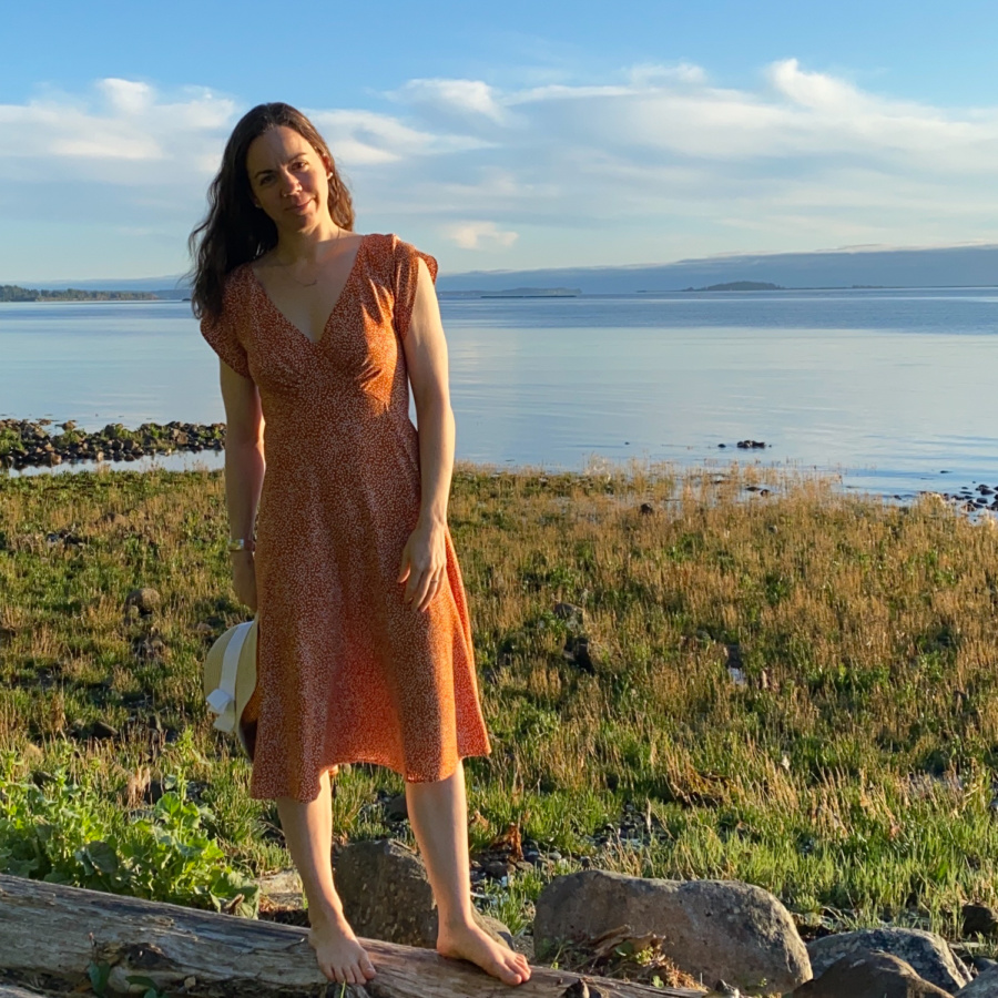 Me standing on a log on the beach with the water behind me, wearing a orange v-neck midi dress