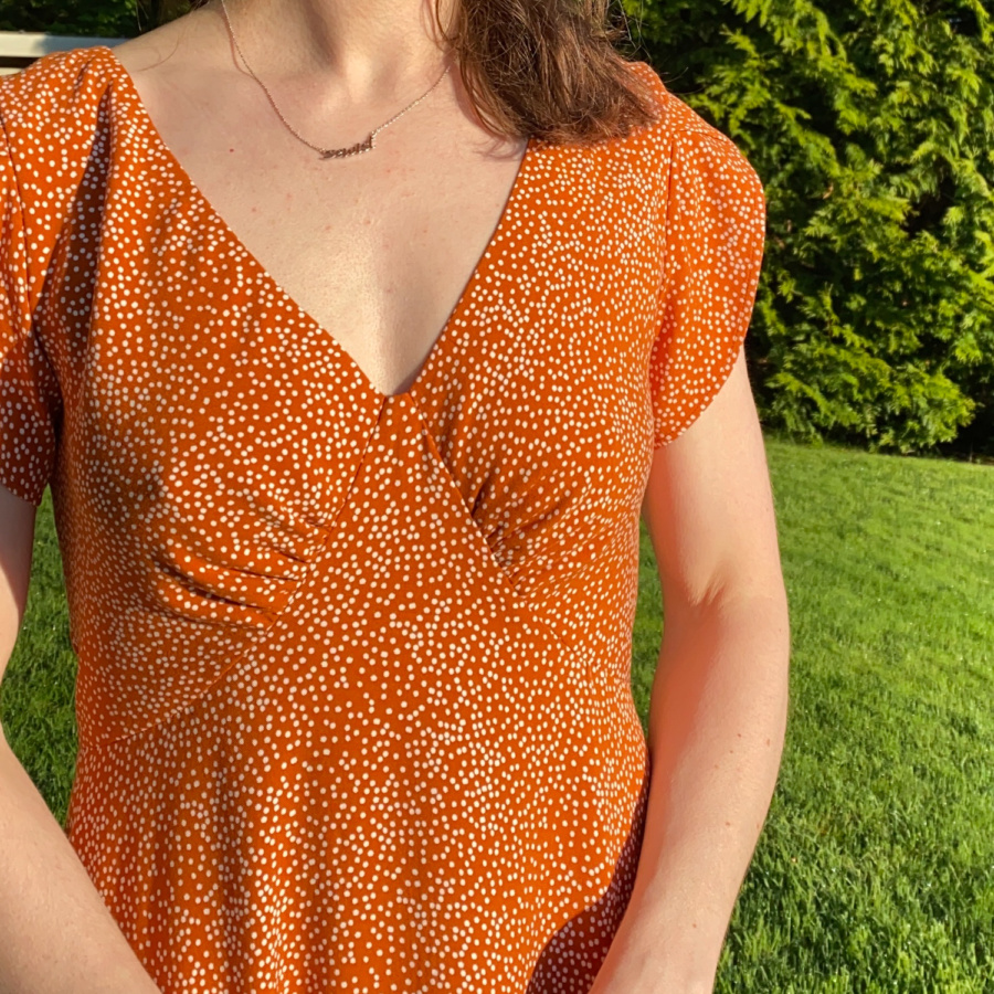 Close up V-neck dress bodice front view. Dress is orange with white polka dots.