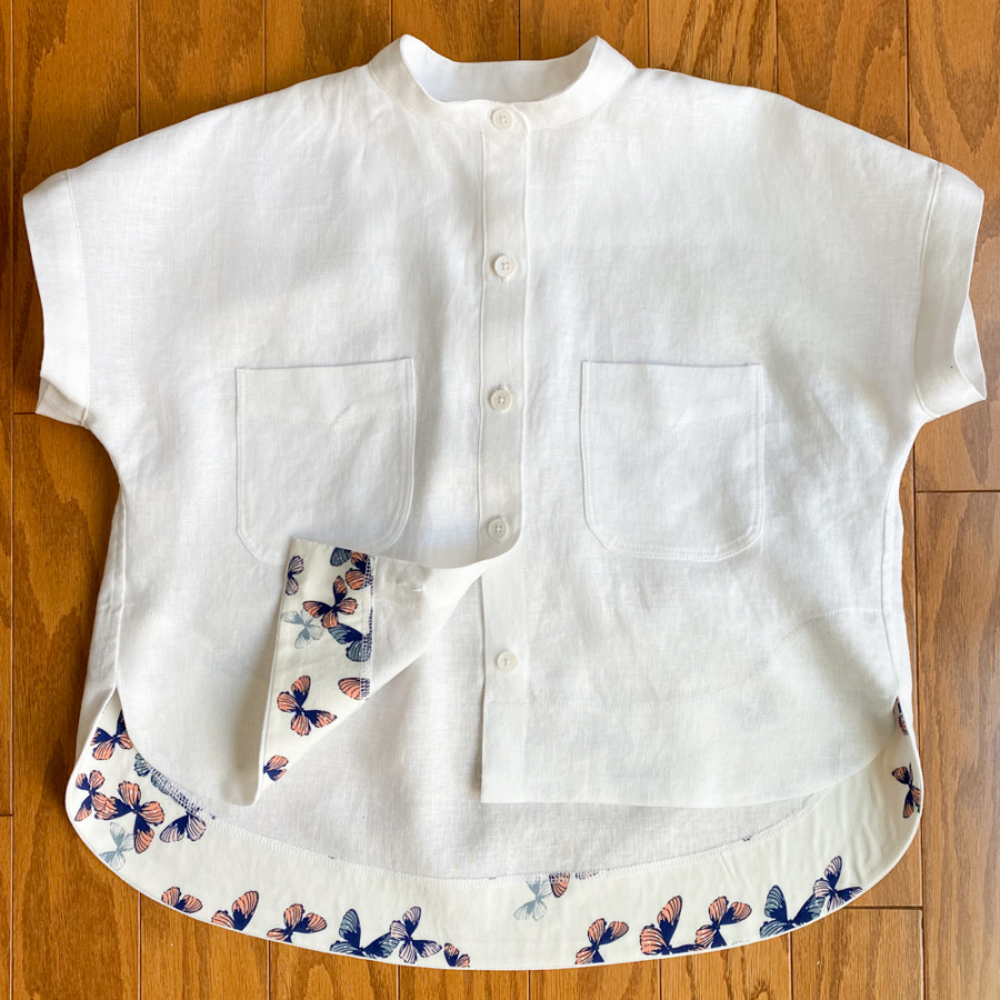 Buttoned white linen Kalle shirt lying on the floor with the butterfly-print facing showing