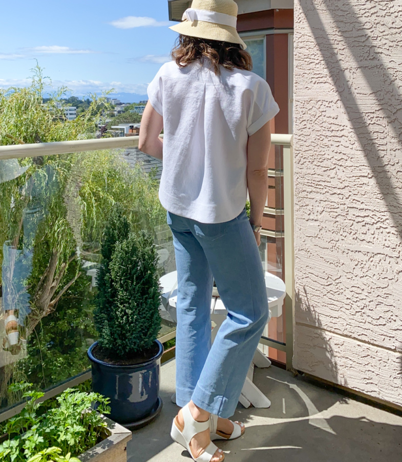 Me standing on a balcony wearing a cropped, white linen Kalle Shirt and blue jeans with my back to the camera.