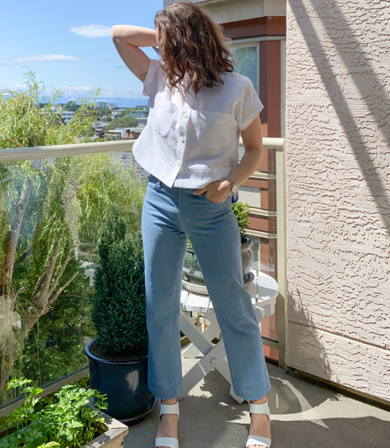Me standing on a balcony wearing a cropped, white linen Kalle Shirt and blue jeans with one hand in my jeans pocket.