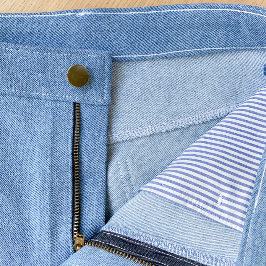 Close up of open front with button, zip and striped pocket bag showing.