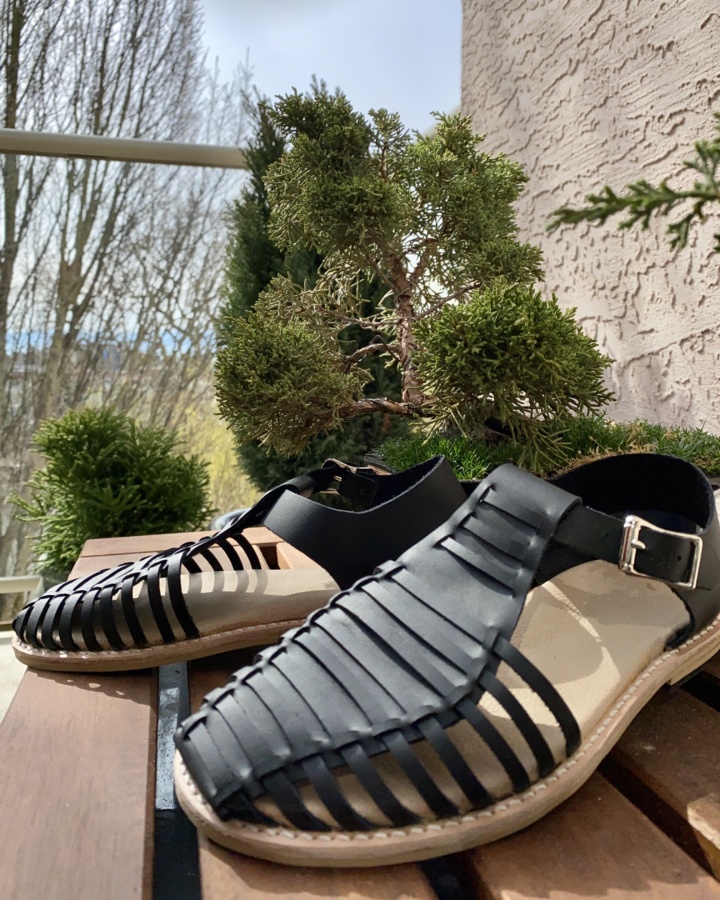 Black leather sandals sitting beside a bonsai tree in the sun