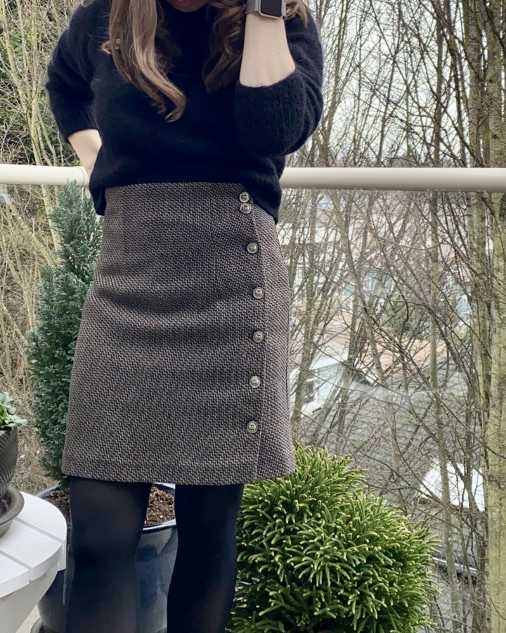 Slightly wider front view of the wool skirt worn with a black sweater and tights. The photo is cropped just below the wearers shoulders and just below the knees. 