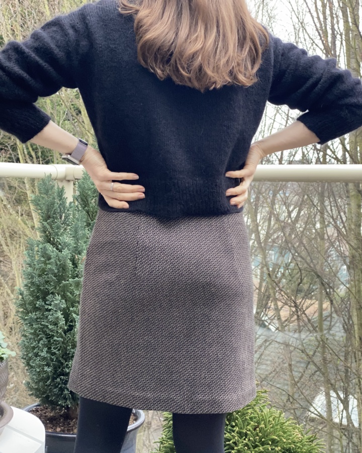 Back view of wool skirt with buttons running down the left side. Worn with a black fuzzy sweater, black tights and hands on hips, fingers facing backward.