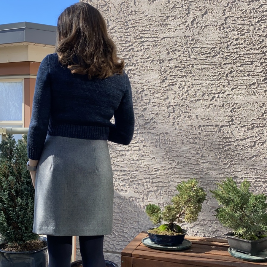 Back view of my outfit - navy blue sweater and grey mini skirt, shown from knees up. Two small bonsai trees behind.