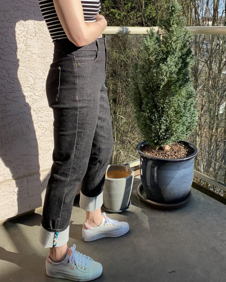 Me wearing my black Brooks Jeans and a black and white striped top. Standing beside a small potted hedge tree. I'm facing sideways to the camera and wearing white runners. Photo shows from my waist down.