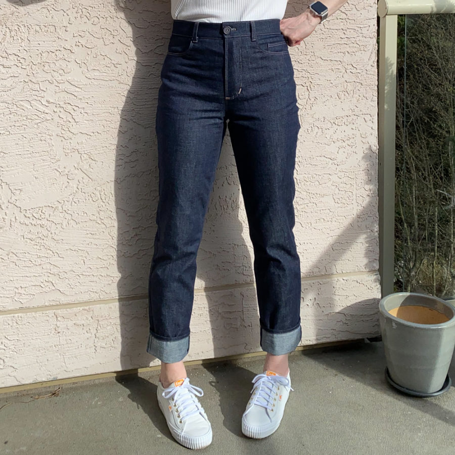 Me wearing my indigo jeans, standing beside a pink wall. Photo is from waist down and I'm facing the camera. I'm wearing a white top and white runners.