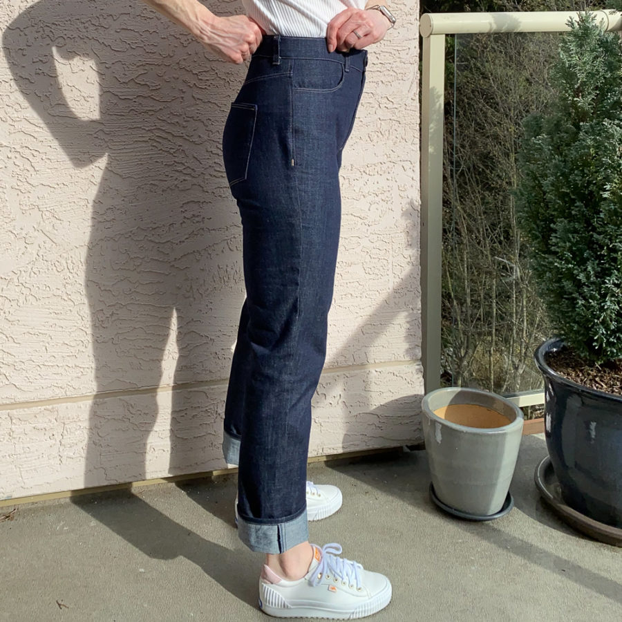 Me wearing my indigo jeans, standing beside a pink wall. Photo is from waist down and I'm facing sideways to the camera with my hands at my waistband. I'm wearing a white top and white runners.