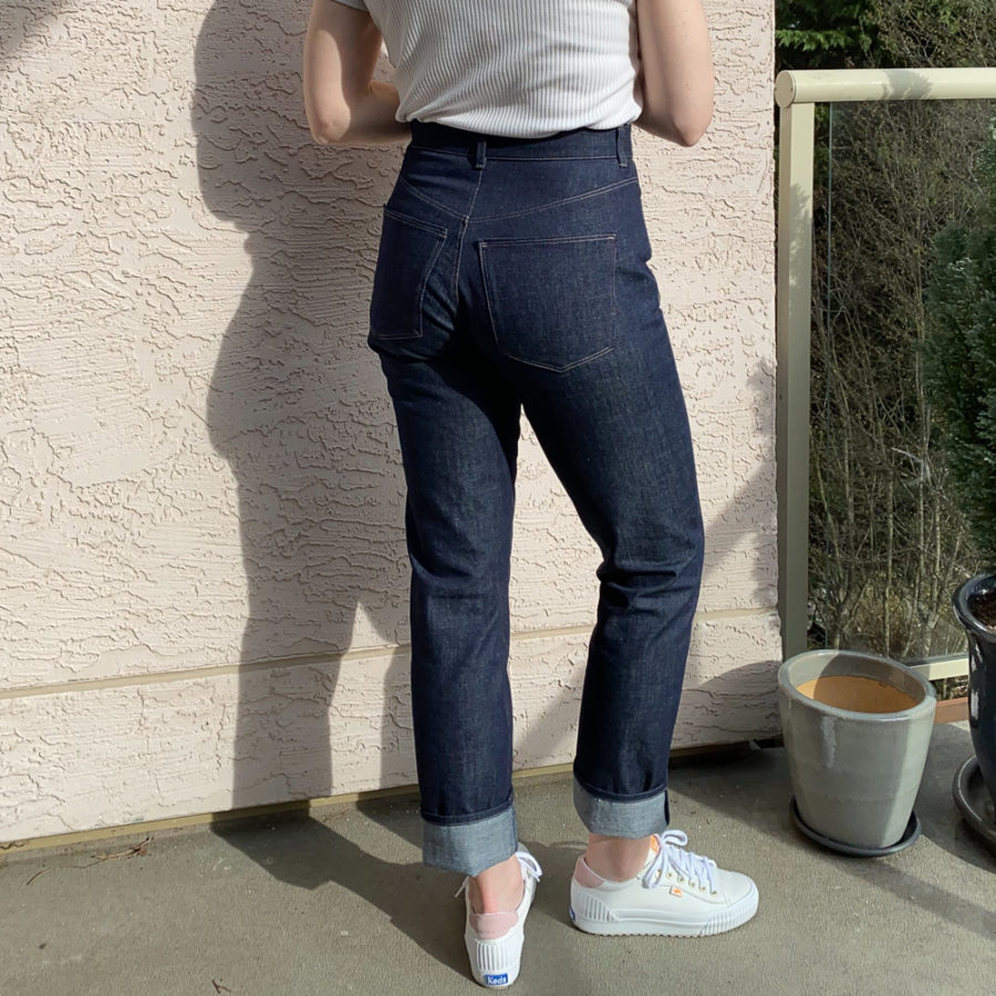 Me wearing my indigo jeans, standing beside a pink wall. Photo is from mid-back down and I'm facing away from the camera. I'm wearing a white top and white runners.